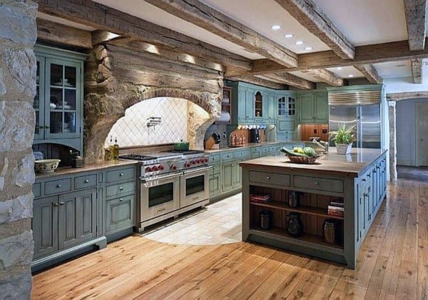 Rustic kitchen with green cabinets, wooden beams, stone accents, and a large island.