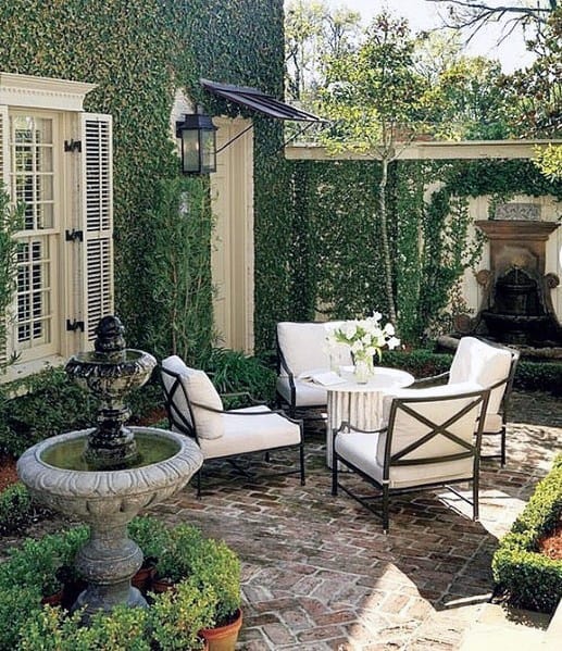 Brick patio with white chairs, a table, fountain, and ivy-covered walls