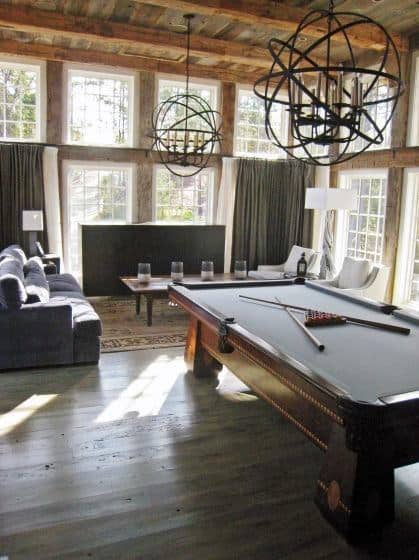 Sunlit game room with a pool table, blue sofa, and large windows, two spherical light fixtures hang from the ceiling