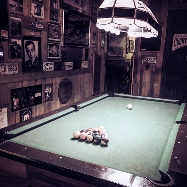 Rustic billiards room with wooden walls, vintage decor, and a classic pool table setup.