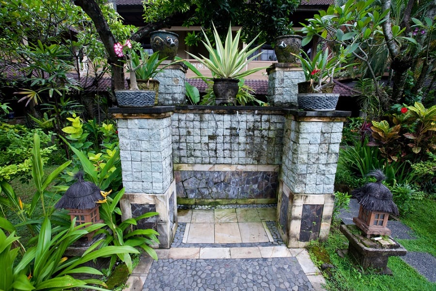 Stone and tile outdoor shower with tropical plants and decorative lanterns.