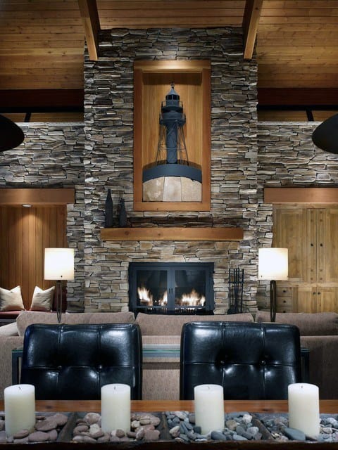 Rustic living room with stacked stone fireplace, wooden mantel, and lighthouse artwork.