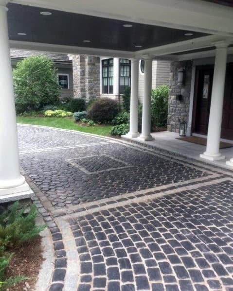 Black cobblestone driveway with gray stone borders, creating a rustic and elegant design.