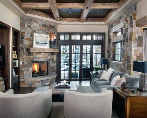 Rustic living room with stone corner fireplace, exposed wood beams, gray sofa, and beige armchairs.