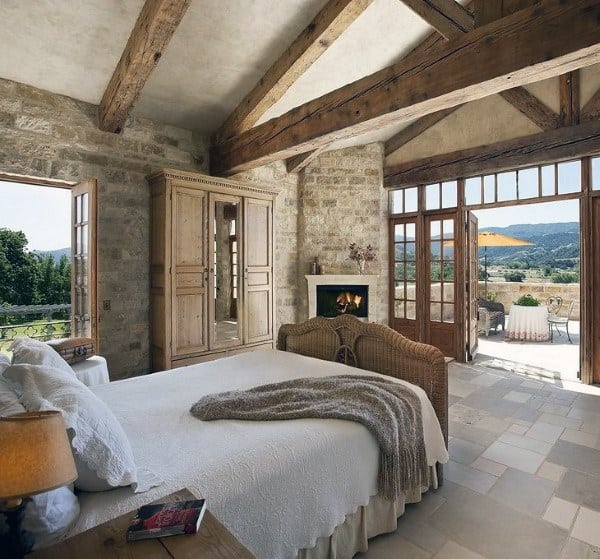 Rustic bedroom with exposed beams, stone walls, fireplace, and patio access.