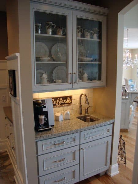 Compact coffee bar with glass cabinet doors, small sink, granite countertop, and coffee maker.