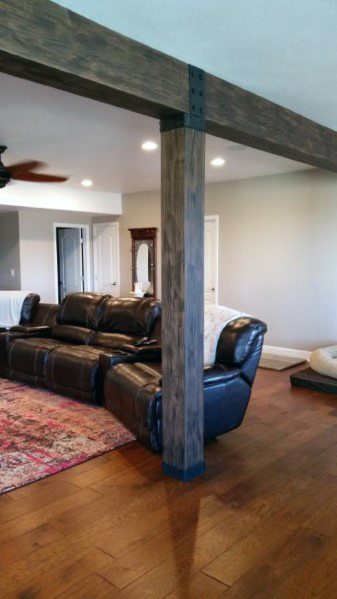 Basement with rustic wood beam pole, leather recliners, and hardwood flooring.
