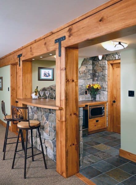 Rustic basement with wooden beams, a stone bar, and stools creating a cozy seating area.