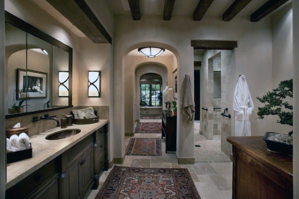 Rustic bathroom with exposed wood beams, arched doorways, double vanity, and stone flooring.