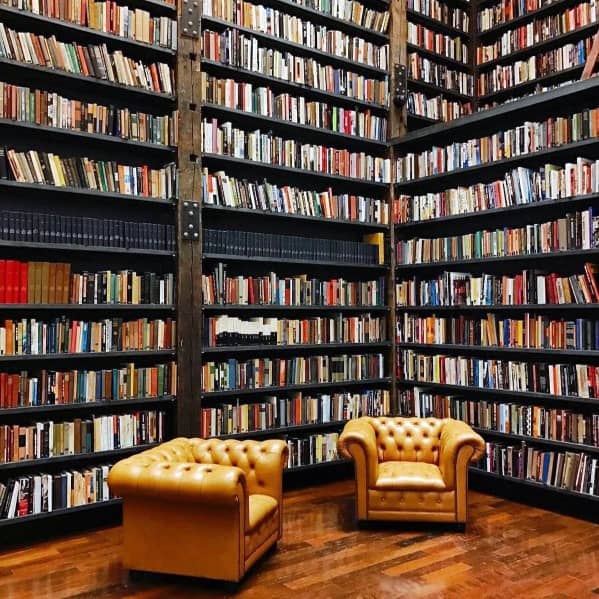 A library with tall bookshelves full of books and two brown leather chairs on a wooden floor
