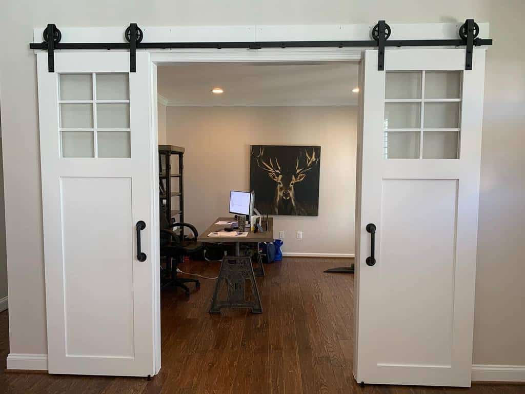 White rustic sliding French barn doors with glass panes and black handles leading to a home office.