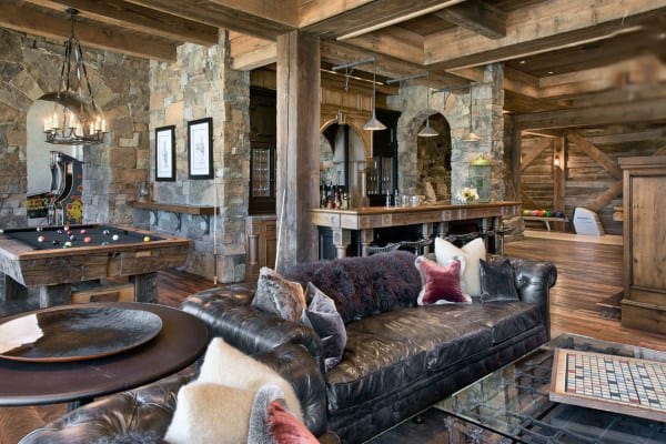 Rustic living room with stone walls, leather couch, pool table, bar area, and wooden beams