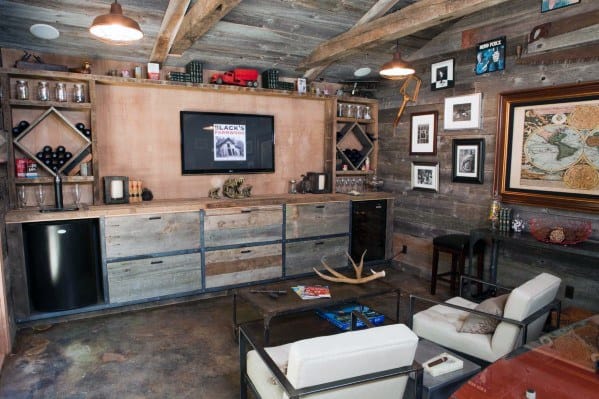Rustic home bar with wood paneling, shelves, art, antlers, and a TV; features seating and various decor items