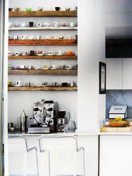 Coffee bar with rustic wooden shelves, colorful mugs, espresso machine, and modern seating.