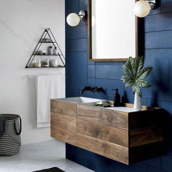 Bathroom with navy shiplap walls, floating wood vanity, round lights, and a triangular shelf.