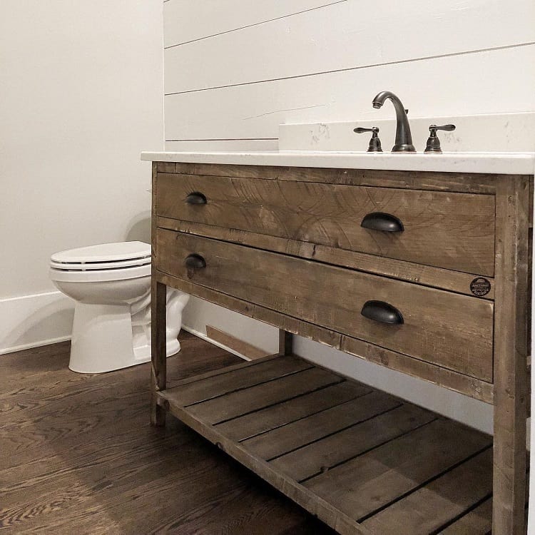 Farmhouse bathroom with a wooden vanity, white sink, and a toilet against white shiplap walls