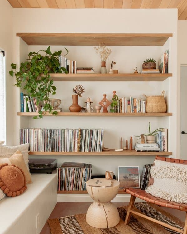 Boho-style living space with wooden floating shelves, plants, books, and a vinyl record collection.