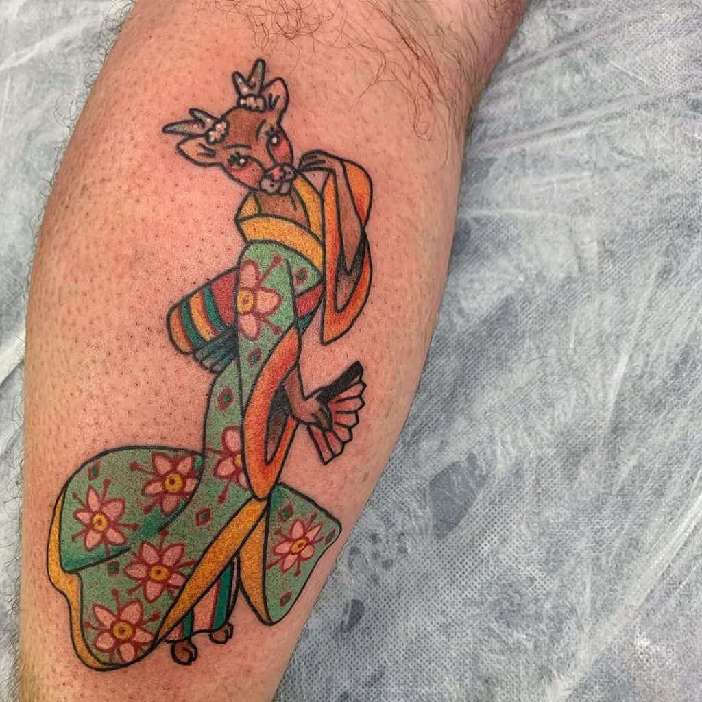Colorful tattoo of a Geisha with a deer’s head, wearing a floral kimono with bright green, orange, and yellow tones in a whimsical design.