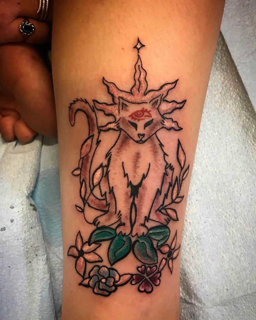 Tattoo of a mystical cat with a third eye, radiating energy, surrounded by vines and flowers, inked in black and red on the forearm.