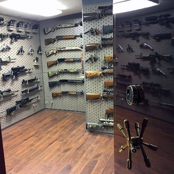 Gun vault with pegboard walls displaying firearms and hardwood flooring.