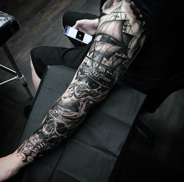 Black and grey full-sleeve tattoo featuring a detailed sailing ship, crashing ocean waves, a skull, and dark shading for a dramatic nautical theme.