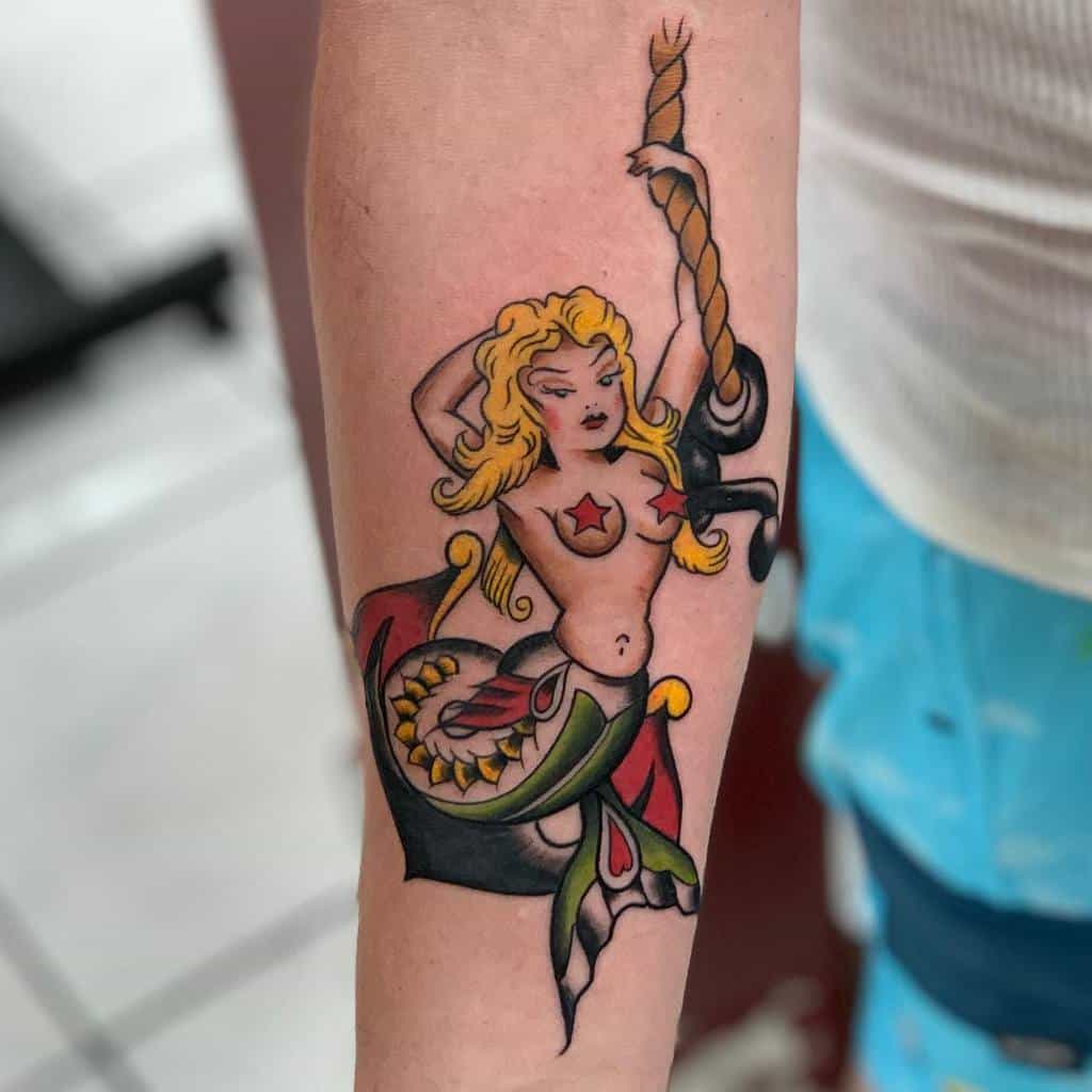 Traditional tattoo of a blonde mermaid with a red star on her chest, holding a rope, with bold colors and classic sailor-style design.