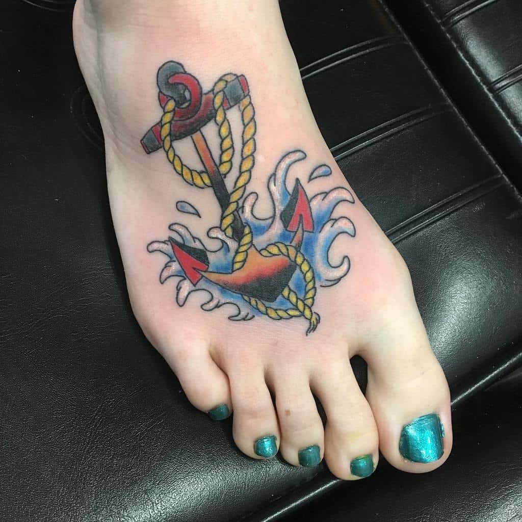 Foot with an anchor and rope tattoo, surrounded by waves, with toenails painted turquoise