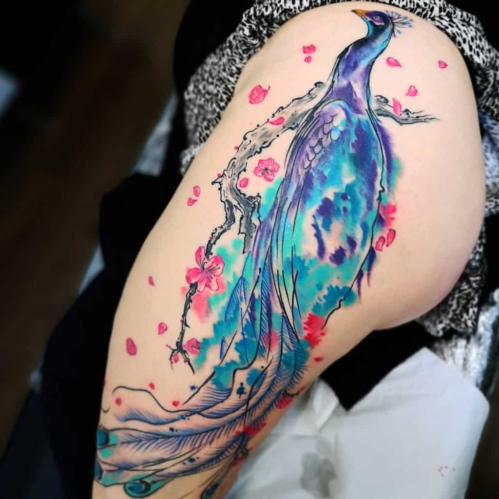 Colorful peacock tattoo with cherry blossoms on upper thigh, showing vibrant blues and purples