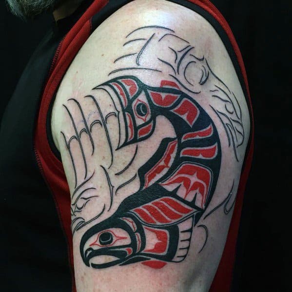 Bold tribal-style salmon tattoo in black and red, inspired by Indigenous art, featuring intricate patterns and flowing lines on the upper arm.