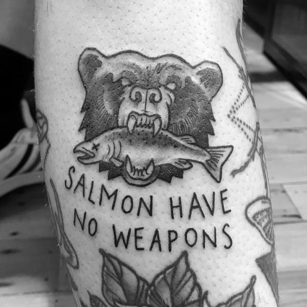Black and grey tattoo of a bear biting a salmon with the phrase "Salmon Have No Weapons," featuring bold outlines and dot shading for a classic look.