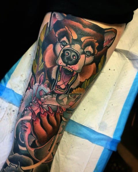 Vibrant tattoo of a fierce bear catching a salmon, featuring bold colors, dynamic shading, and intricate details for a powerful full-leg design.