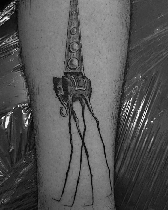 Black and grey tattoo of a surreal Salvador Dali-style elephant with ultra-long legs and a tall, patterned obelisk balanced on its back.
