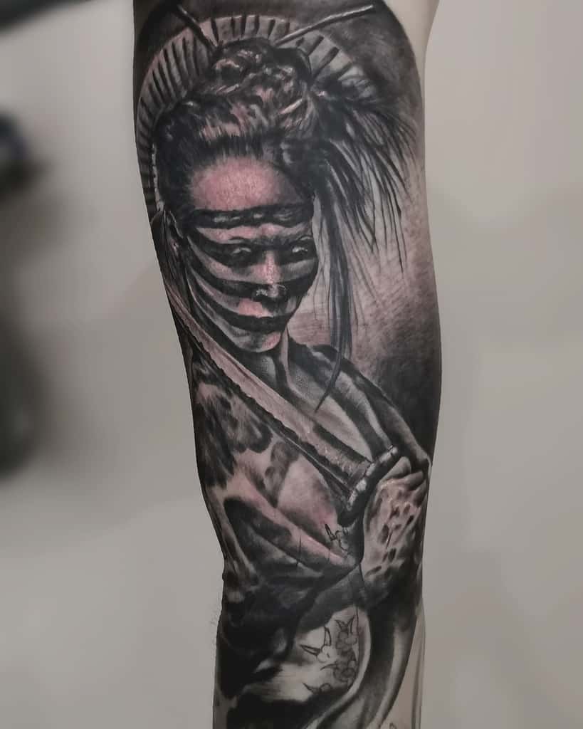 Dark and surreal black and gray tattoo of a Geisha with a blindfold-like effect, holding a sword, featuring intense shading and eerie details.