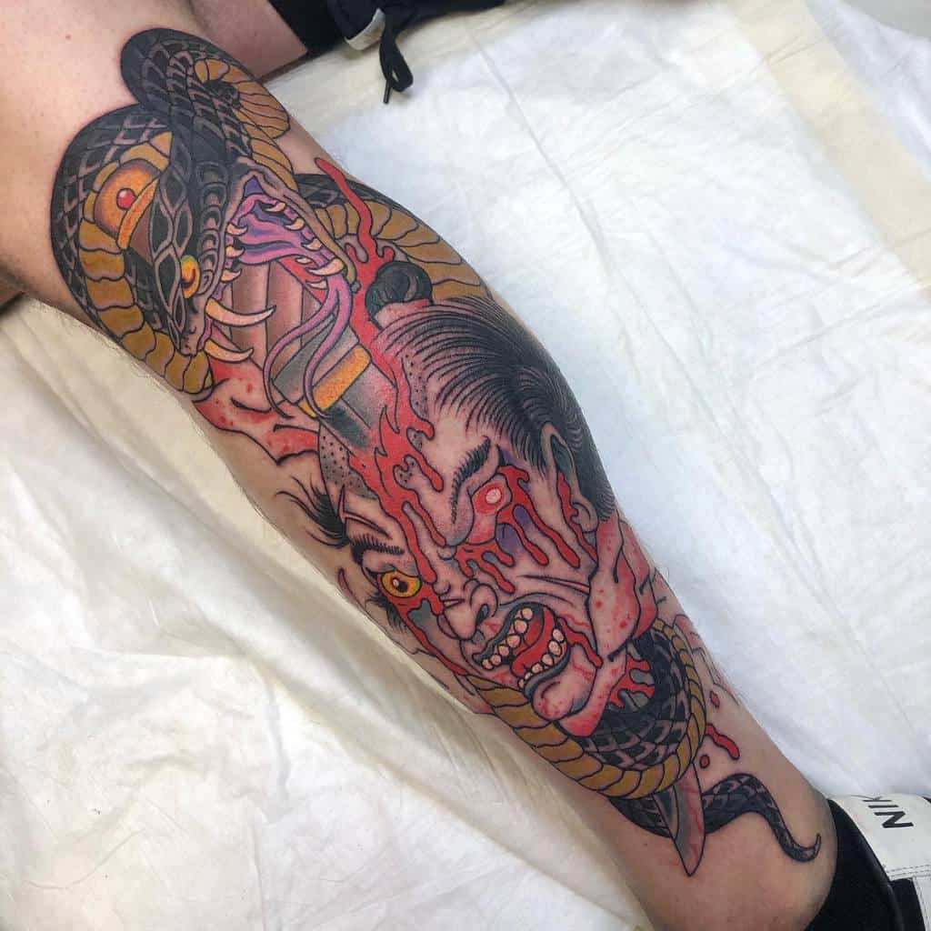 Vibrant leg sleeve tattoo featuring a snake intertwining with a fierce, blood-spattered samurai face in a bold, traditional style