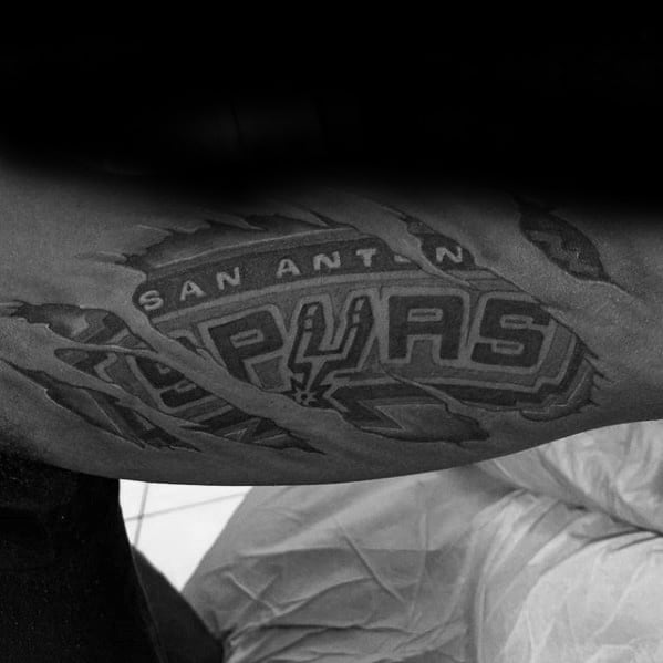Realistic torn skin tattoo revealing the San Antonio Spurs logo in black and gray on the inner bicep, with detailed shading and depth.