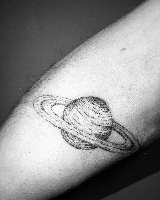 Minimalist Saturn tattoo design for men with fine dotwork detailing and textured ring lines placed on the inner forearm.