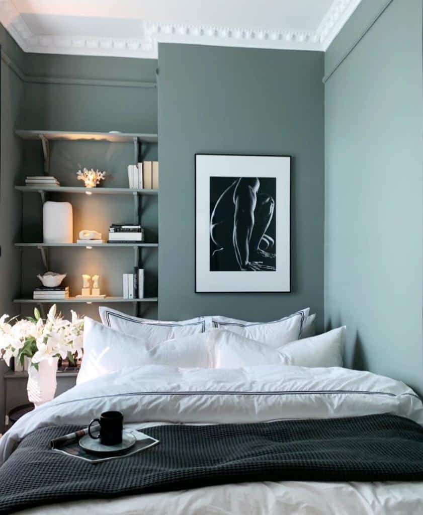 Scandinavian bedroom with green walls, white bedding, and minimalist shelves for decor.