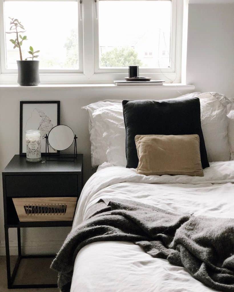 Cozy bedroom with black nightstand, neutral bedding, and decorative pillows by the window.