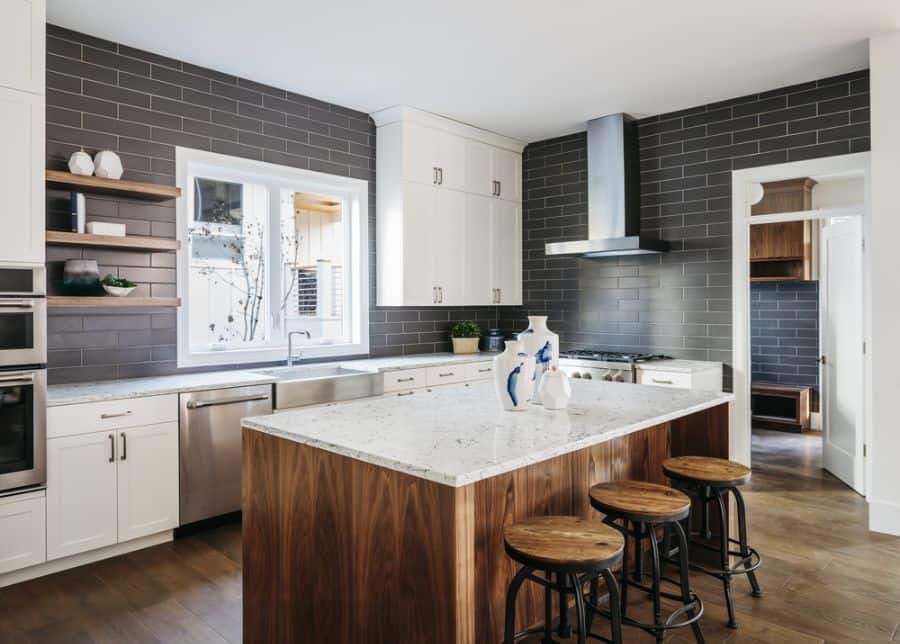 Modern kitchen with white cabinets, dark tile backsplash, and wooden island with stools.