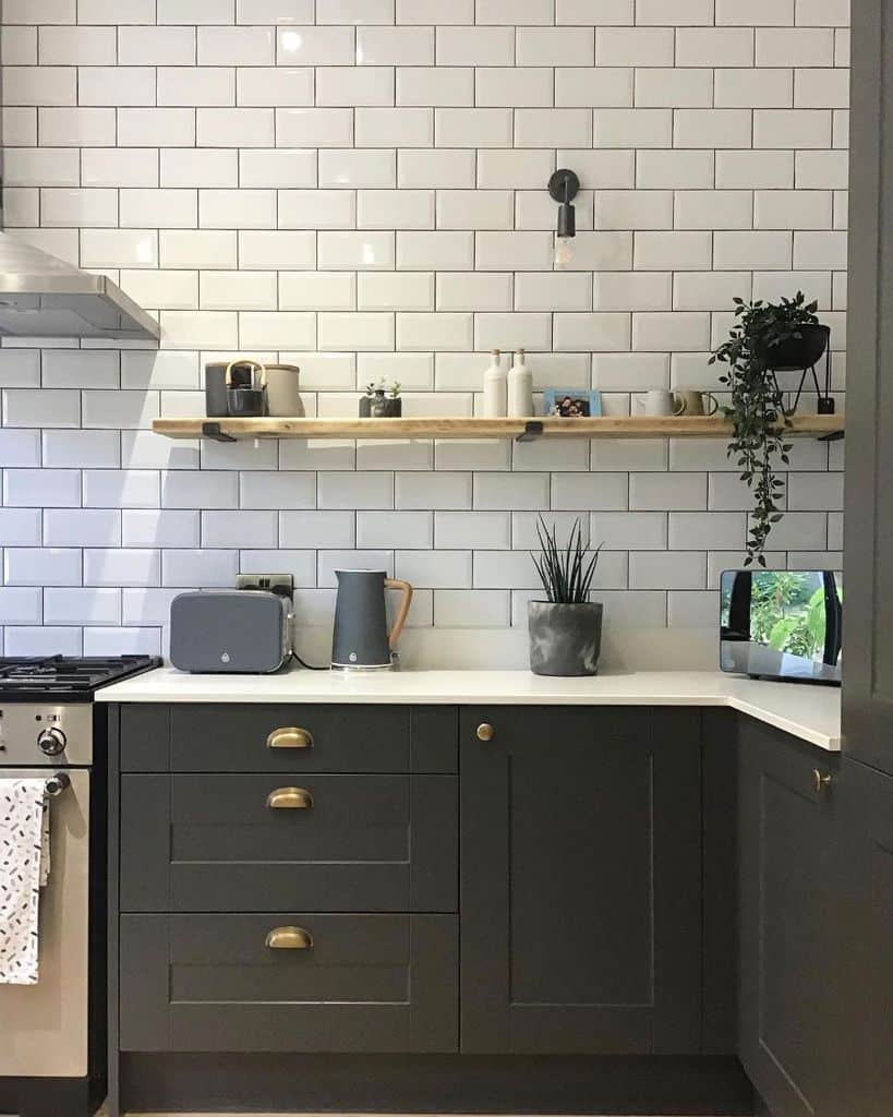 Black kitchen cabinets with white subway tiles and a wooden shelf.