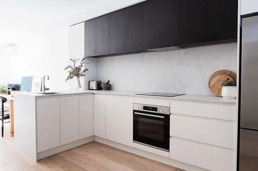 Scandinavian kitchen with black and white cabinets, built-in oven, and light wood flooring.