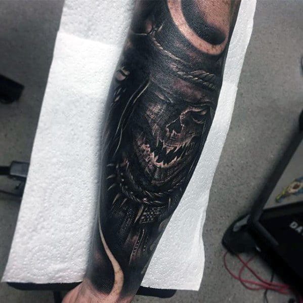 Dark and detailed scarecrow tattoo on the forearm with a sinister stitched grin, rope details, and intense black and grey shading.