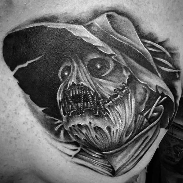 Black and grey scarecrow tattoo with glowing eyes, torn stitched mouth, and flowing hood, creating a haunting and shadowed look.