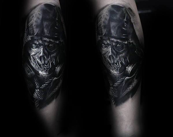 Dark scarecrow tattoo with a stitched skeletal face, intense eyes, hooded cloak, and dramatic black and grey shading on the forearm.