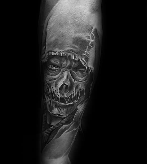 Realistic scarecrow tattoo with a torn stitched mask, intense eyes, and dramatic black and grey shading covering the forearm.