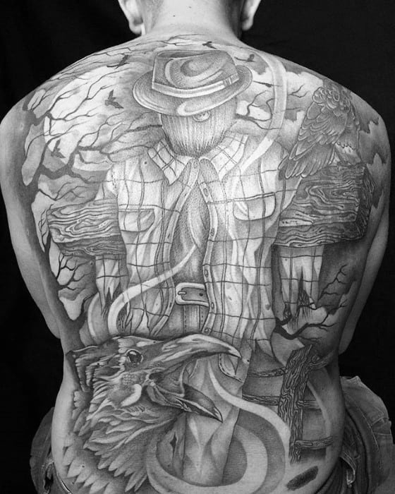 Full back scarecrow tattoo with stitched face, plaid shirt, wide-brim hat, crows, bare trees, and a spooky fence in detailed black and grey.