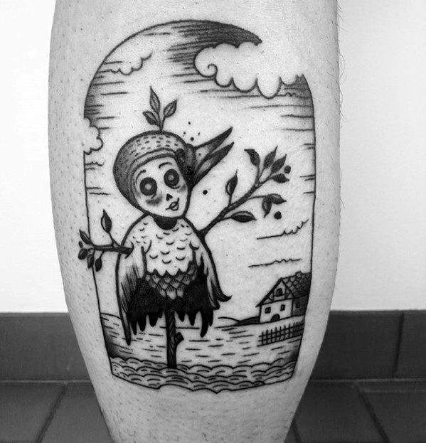 Whimsical blackwork scarecrow tattoo with a stitched doll-like face, leafy arms, a bird on its head, and a house in the background.