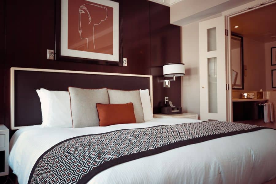 Hotel-style bedroom with dark wood paneling patterned bedding and modern wall sconces.