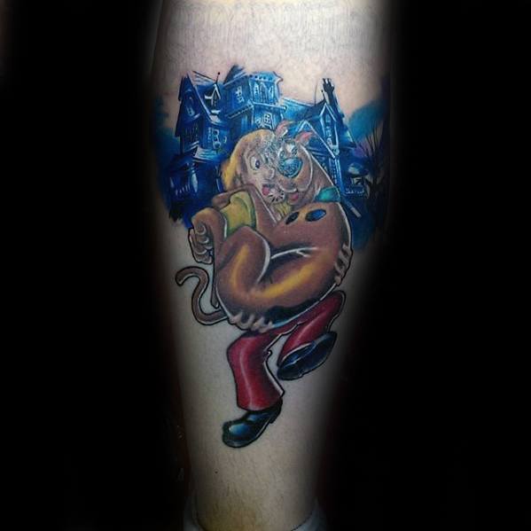 Tattoo of Scooby-Doo dressed as Shaggy, looking scared in front of eerie blue haunted houses with glowing windows.