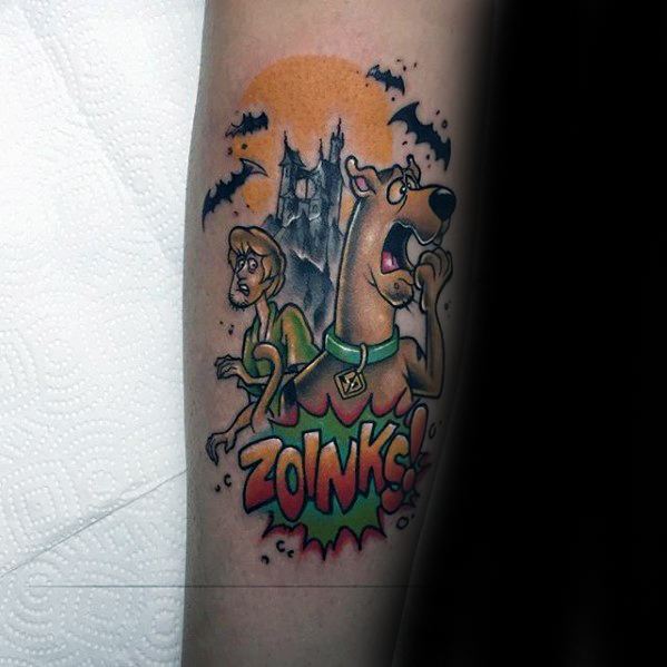 Tattoo of a frightened Scooby-Doo and Shaggy with bats, a haunted tower, and the word “ZOINKS!” in bold comic-style text.
